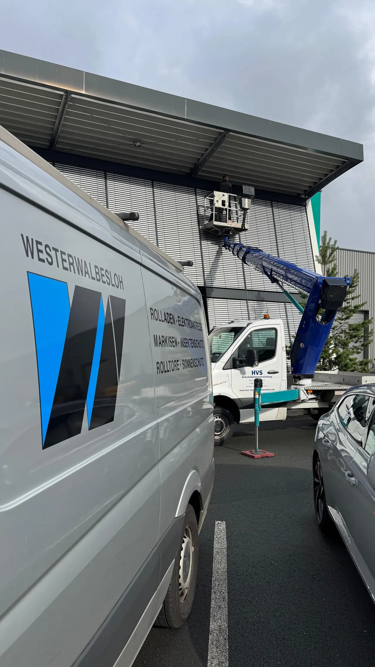 Firmenwagen von Westerwalbesloh vor einer Halle, dahinter ein Hubsteiger bei der Arbeit an der Fassade