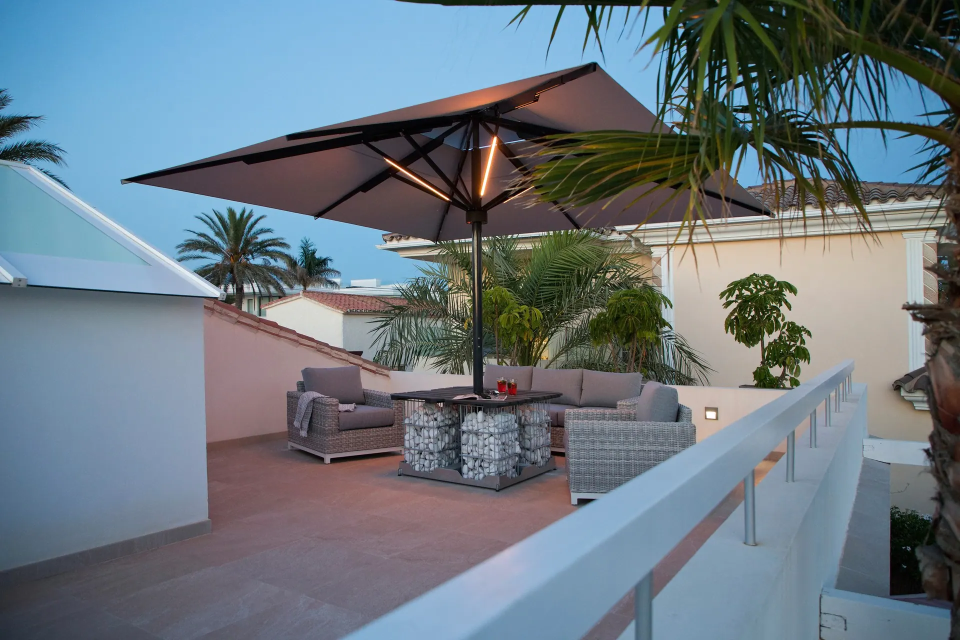 Sonnenschirm mit Beleuchtung über einer Dachterrasse mit Loungemöbeln in der Abenddämmerung